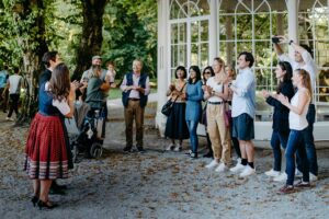 A vibrant group of tourists is gathered around a gazebo in Hellbrunn, clapping and enjoying a performance by the spirited Dana and Dmitry during a memorable show on a Private Sound of Maria Tour.