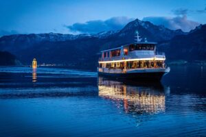 A ship on Lake Wolfgang at night, surrounded by towering mountains in the dark.