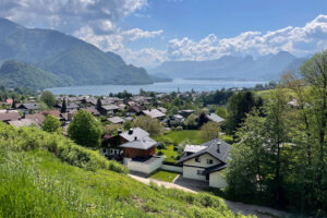 Overlooking the idyllic Salzkammergut Lake District, the viewpoint reveals a tapestry of lush greenery, charming homes, and the serene expanse of a sparkling lake set against the backdrop of majestic mountains.