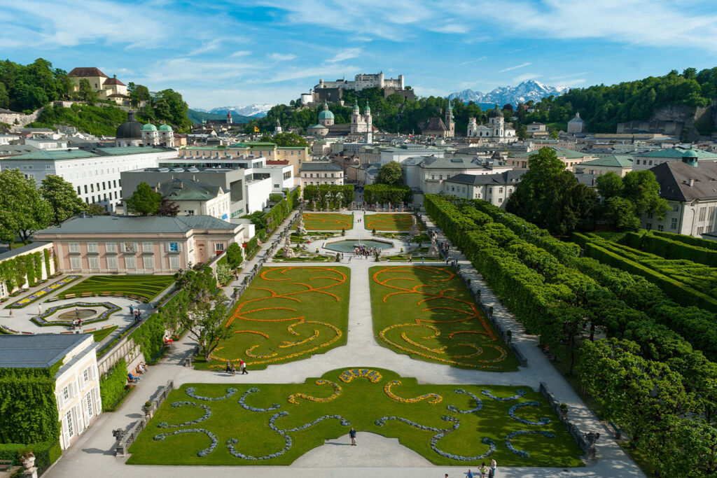The vibrant Mirabell Gardens in Salzburg, a scene of jubilant melodies and dance in the finale of the tour under the gaze of the majestic Hohensalzburg Fortress.