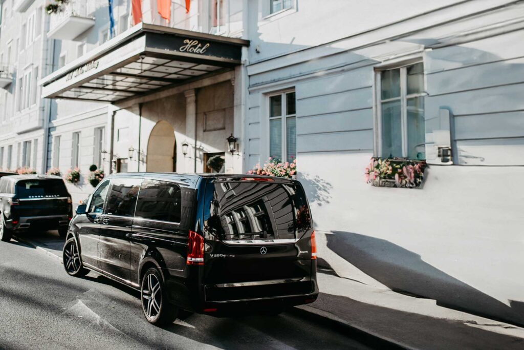 A black luxury van is parked in front of a hotel, ready to welcome guests for the "Private Sound of Maria Tour" in Salzburg.