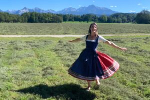A woman joyfully twirls in a traditional dress against the stunning backdrop of the Austrian Alps, embodying the spirit of the hills that come alive with music on the Private Sound of Maria Tour.