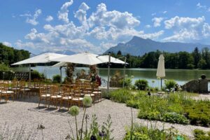 The terraces of Schloss Leopoldskron, dappled in sunlight, set before a tranquil lake and the dramatic backdrop of Salzburg's mountains, a historical location where melodies of a timeless musical were once filmed.