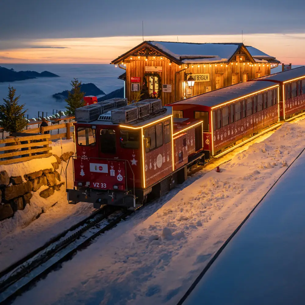 Twilight view of the Singing Xmas Tour Advent Train on Schafberg, with Salzburg’s scenic Christmas lights and mountain views.